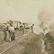 Men burning grass in ditch near railroad tracks