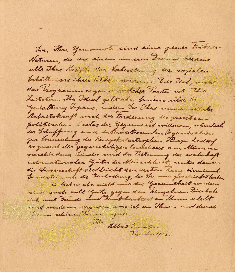 This yellowed letter by Einstein is written in a looped, cursive German calligraphy. Gold dust is scattered over it in concentrated blotches.  