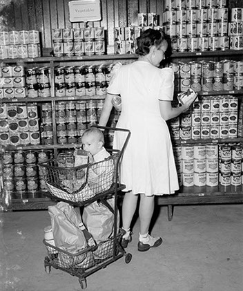 Woman buying canned goods in commissary with baby in shopping cart