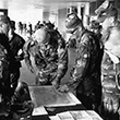 Military personnel hover around a map